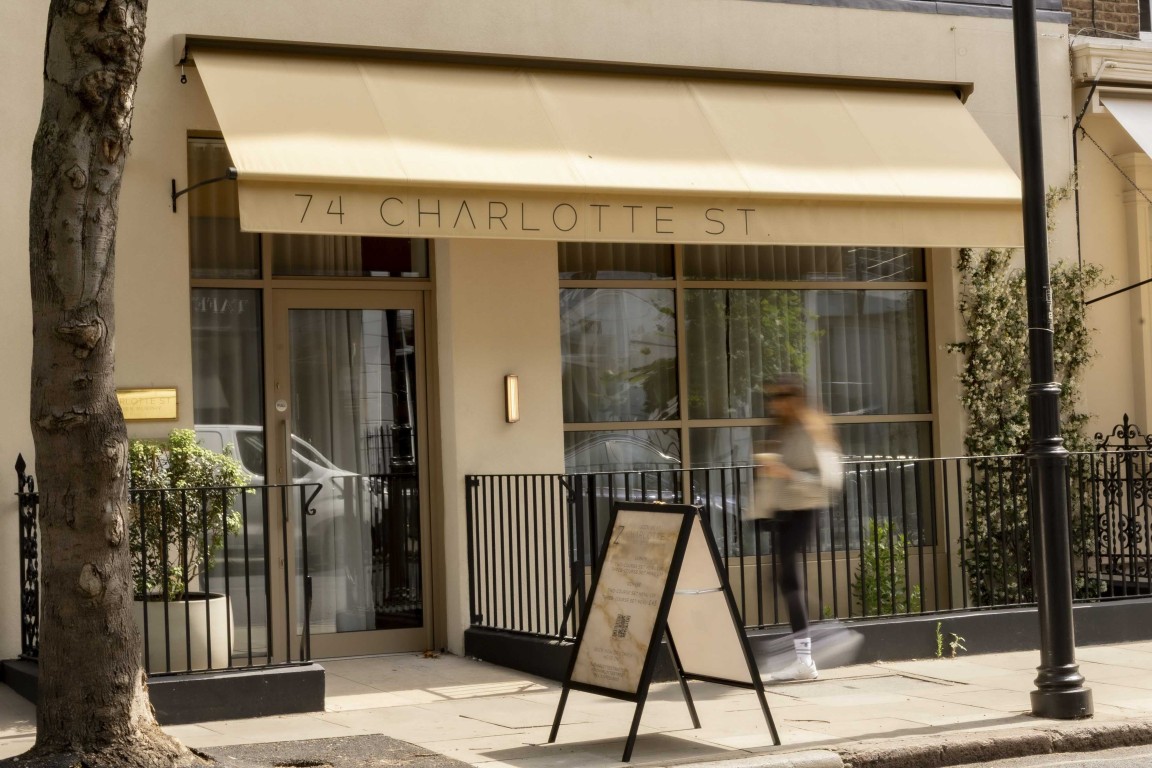 Exterior of 74 Charlotte Street restaurant in Fitzrovia, London, showing its cream awning, glazed entrance and street-facing windows.
