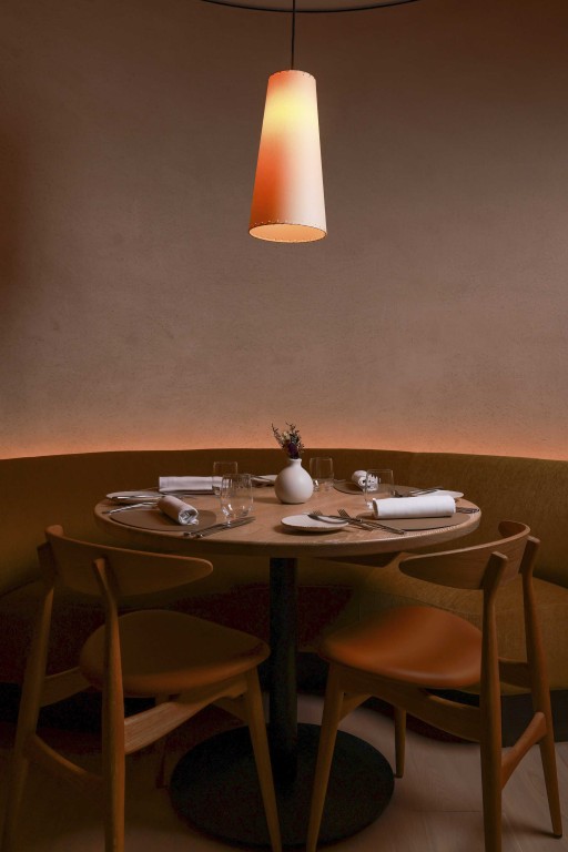 Close-up of a dining alcove at 74 Charlotte Street, with textured Armourcoat Clay Lime Plaster, a curved upholstered banquette and timber furniture.