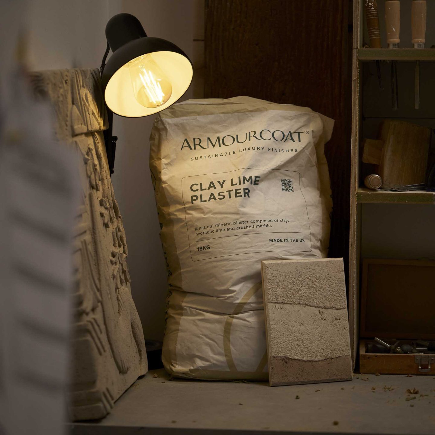 Armourcoat Clay Lime Plaster bags and textured plaster samples displayed in a workshop beside application tools.