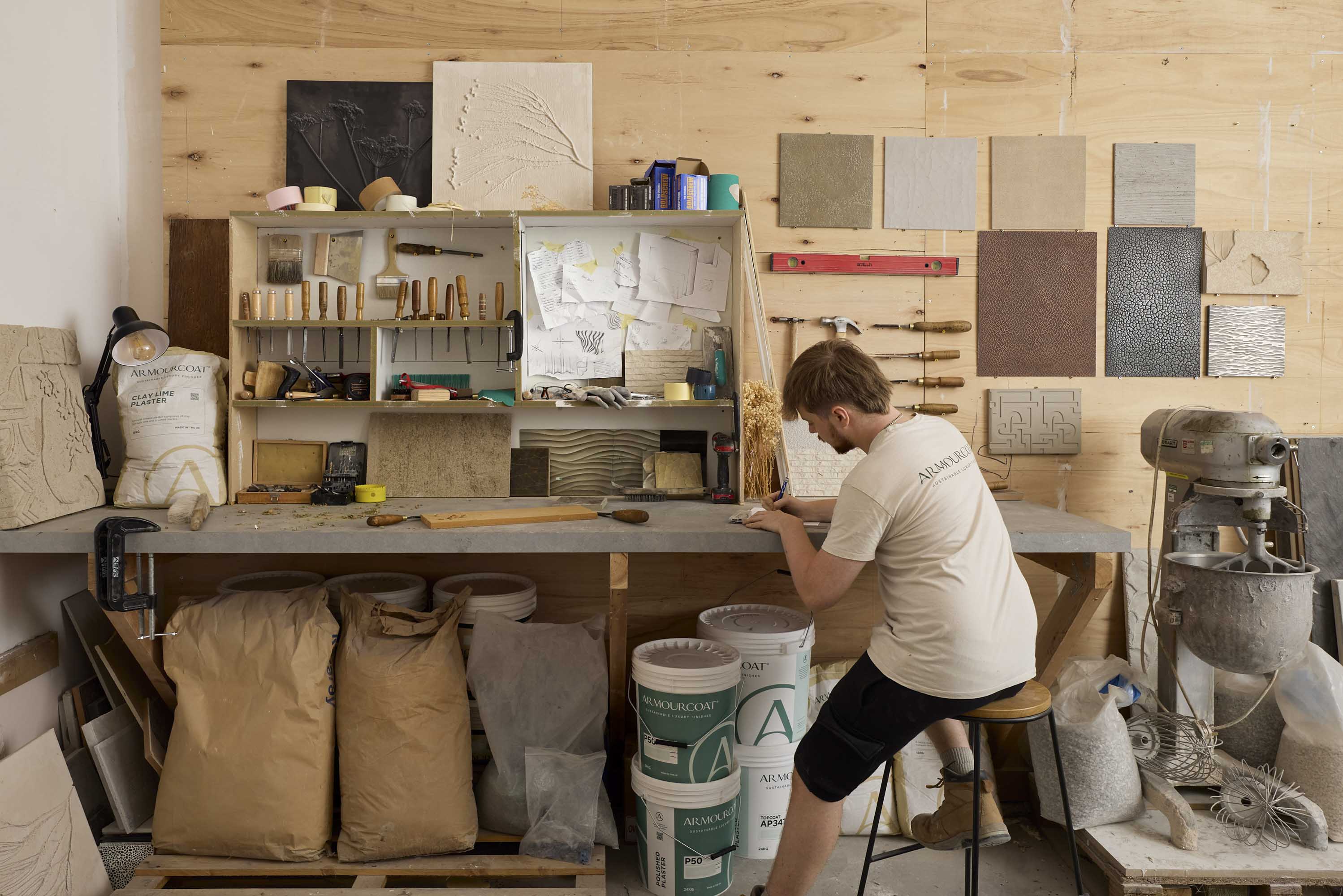 Armourcoat craftsman working at a workshop bench surrounded by tools, materials and decorative surface samples.