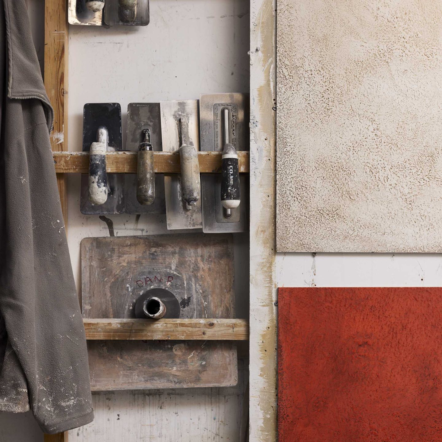 Armourcoat workshop wall with plastering tools, material samples and textured finish panels in neutral and red tones.