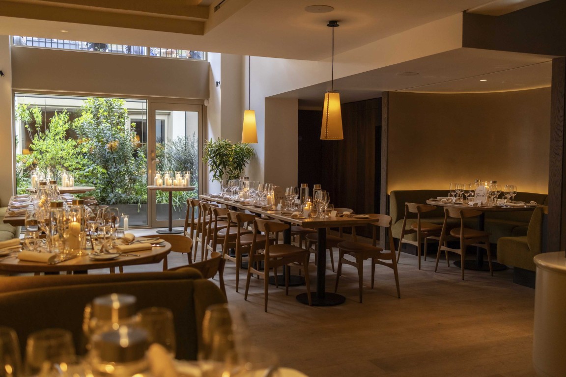 Interior of 74 Charlotte Street restaurant in Fitzrovia, featuring Armourcoat plaster finishes, warm timber furniture, pendant lighting and garden views.