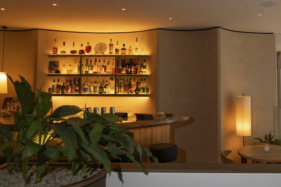 Bar area at 74 Charlotte Street featuring curved architectural walls, illuminated drinks shelving and warm neutral finishes.